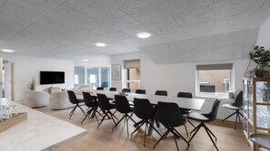 A modern conference room with a long table, black chairs, a TV, and a large window.