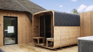 Een houten sauna met een glazen deur, een bankje binnenin en een rieten dak.