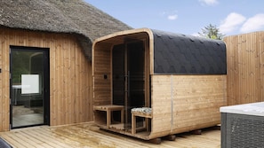 Eine Saunahaus aus Holz mit Glastür, einer Sitzbank im Inneren und einem Reetdach.