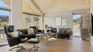 A modern living room with a large window, a black leather sofa, a coffee table, and a television. - VillaVilla 660 - Henne Strand, Vestjylland (Henne)