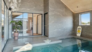 A modern indoor swimming pool with a glass wall, a potted plant, and a surfboard with a smiley face. - VillaVilla 660 - Henne Strand, Vestjylland (Henne)