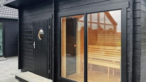 A modern building with a black exterior, a large glass door, and a wooden bench outside.