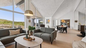A spacious living area with a large window, a dining table, and a kitchen area.