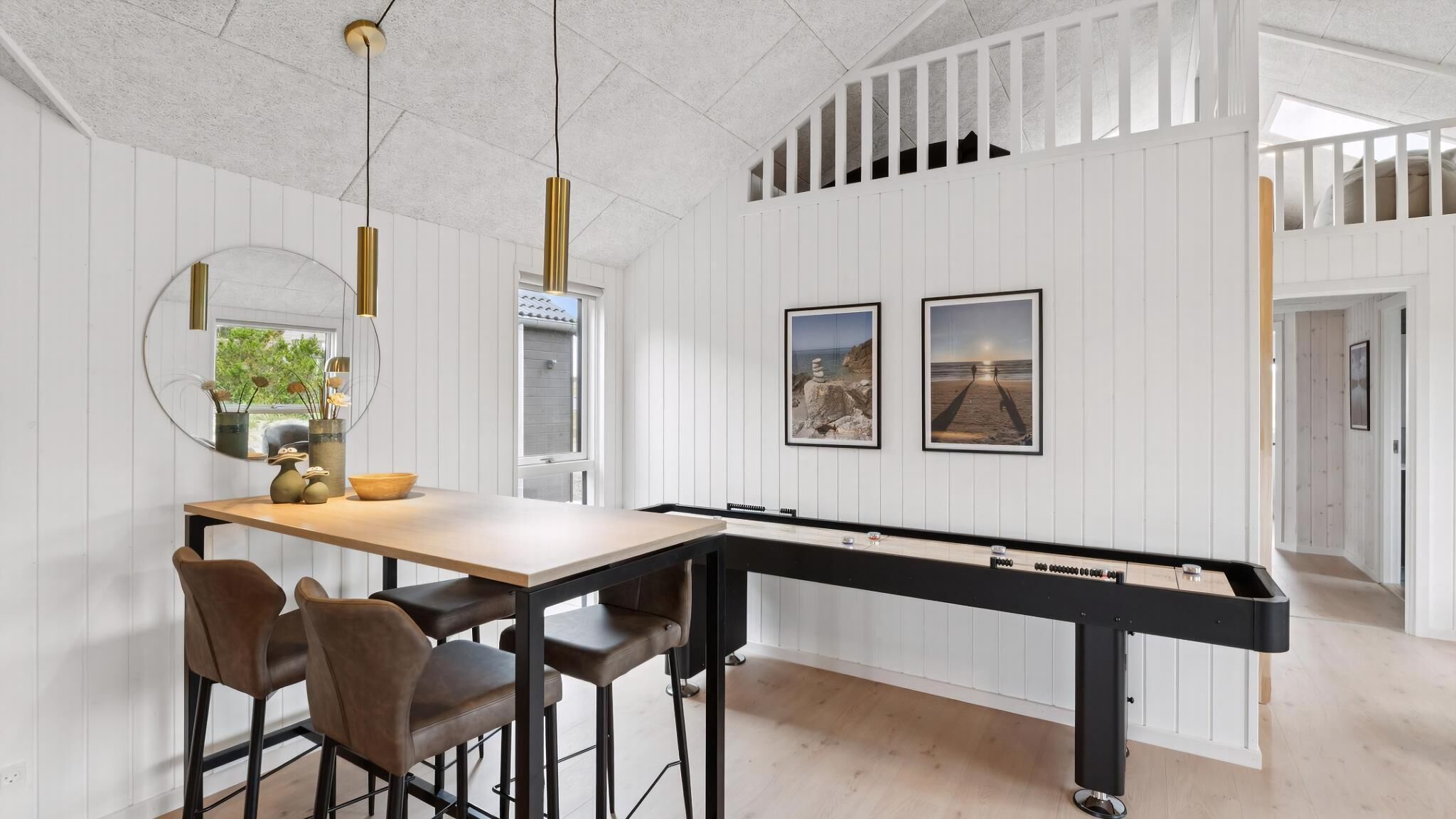 A pool table with a long rail, a dining area with chairs, a mirror, and two framed pictures on the wall.