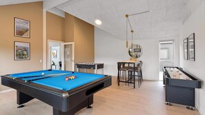 Uma mesa de bilhar, uma mesa de futebol de mesa e um bar com banquetas.