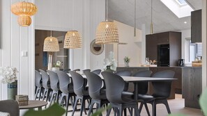 Un espace de salle à manger moderne, avec une longue table, de nombreuses chaises et des luminaires suspendus.