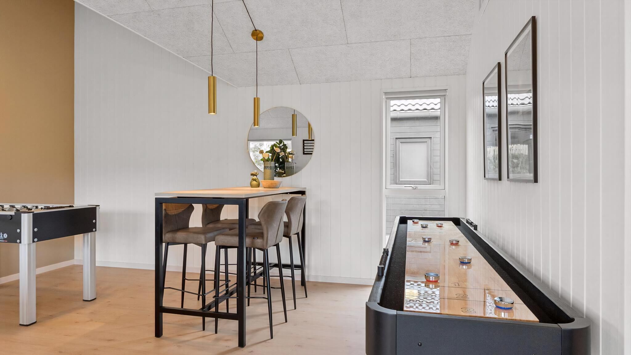 Um quarto com mesa de pebolim, área de bar com banquetas e mesa de jantar com cadeiras.