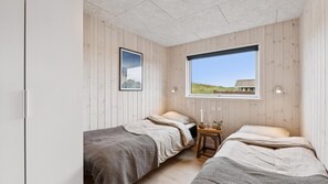 Une chambre avec deux lits, une fenêtre donnant sur la plage, un tableau encadré au mur et une petite table avec une bougie.