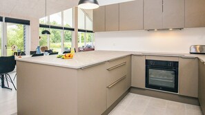 Een moderne keuken met een groot schiereiland, een ingebouwde oven en veel natuurlijk licht door grote ramen.