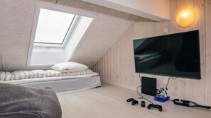 Ein Schlafzimmer im Loft-Stil mit schrägem Dach, einem großen Fernseher und Spieleequipment.