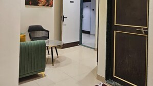 Un pasillo con un sofá verde, una mesita, un cuadro y una puerta que da a un baño.