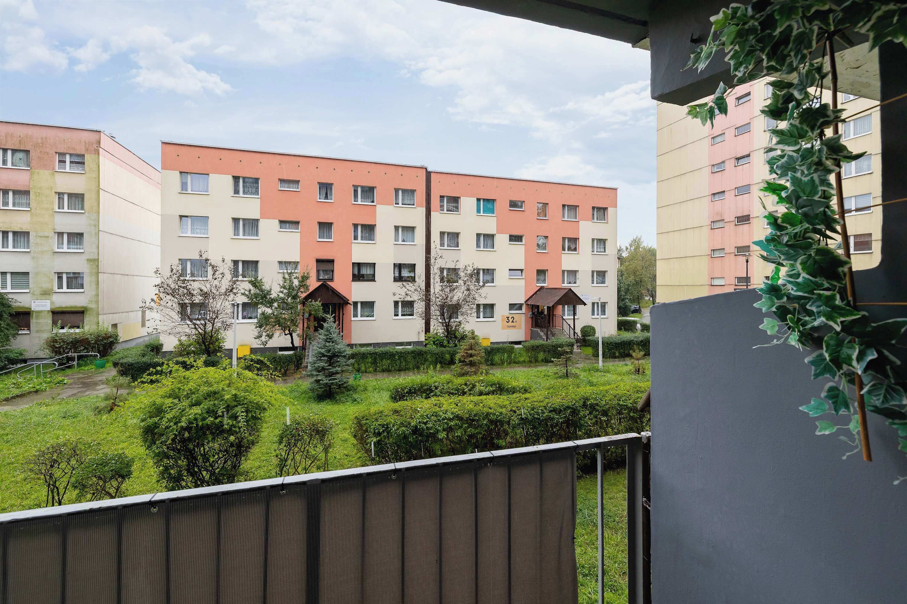 A multi-story residential building with balconies, a small garden area, and a visible entrance.