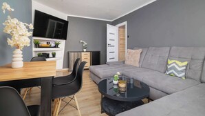 Ett modernt vardagsrum med en grå soffa, svarta stolar, ett matbord i trä och en platt-TV som är monterad på väggen.