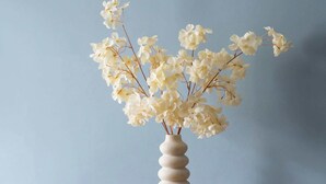 Ett matbord med en vas med vita blommor, en träklocka och svarta stolar.