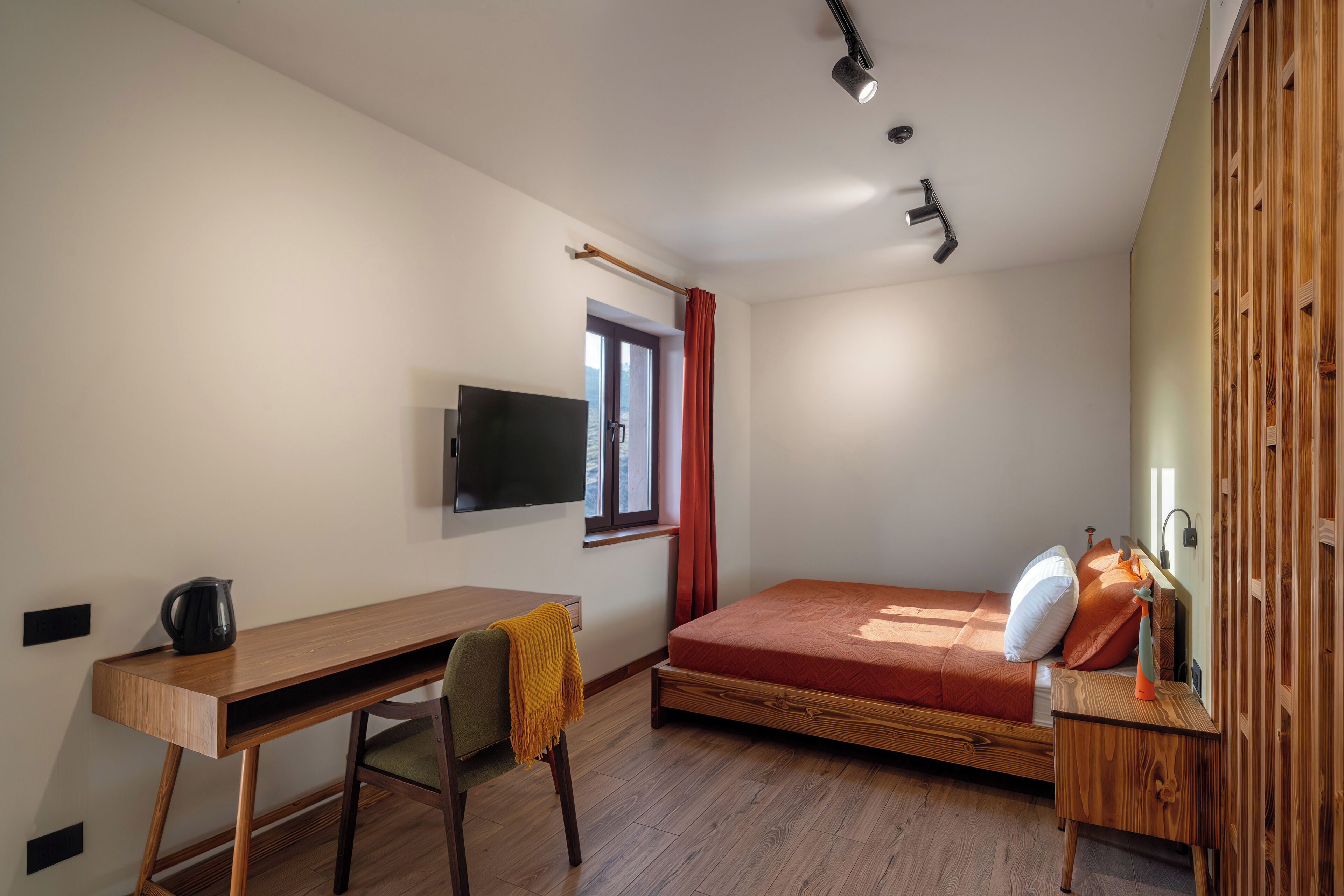 A compact room with a bed, a desk, a chair, a TV, and a window with curtains.