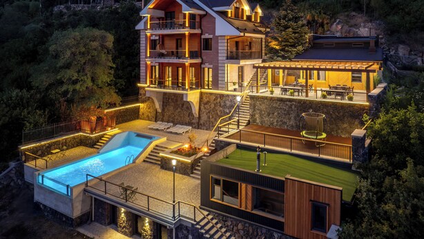 Una casa de varios niveles con piscina, mobiliario exterior y un muro de contención de piedra.
