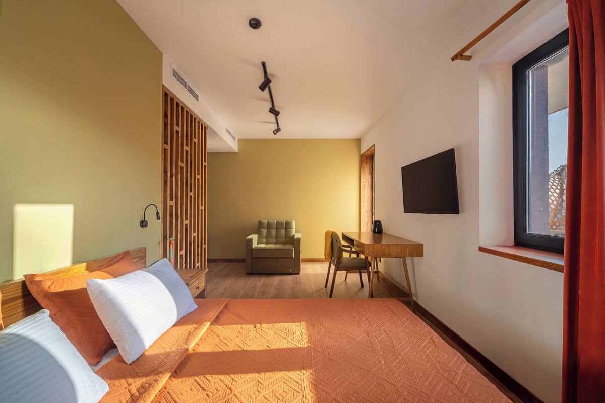 A hotel room with a bed, a desk, a chair, a television, and a window.