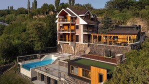 Una casa de varios pisos con piscina, terraza de madera y un muro de contención de piedra.