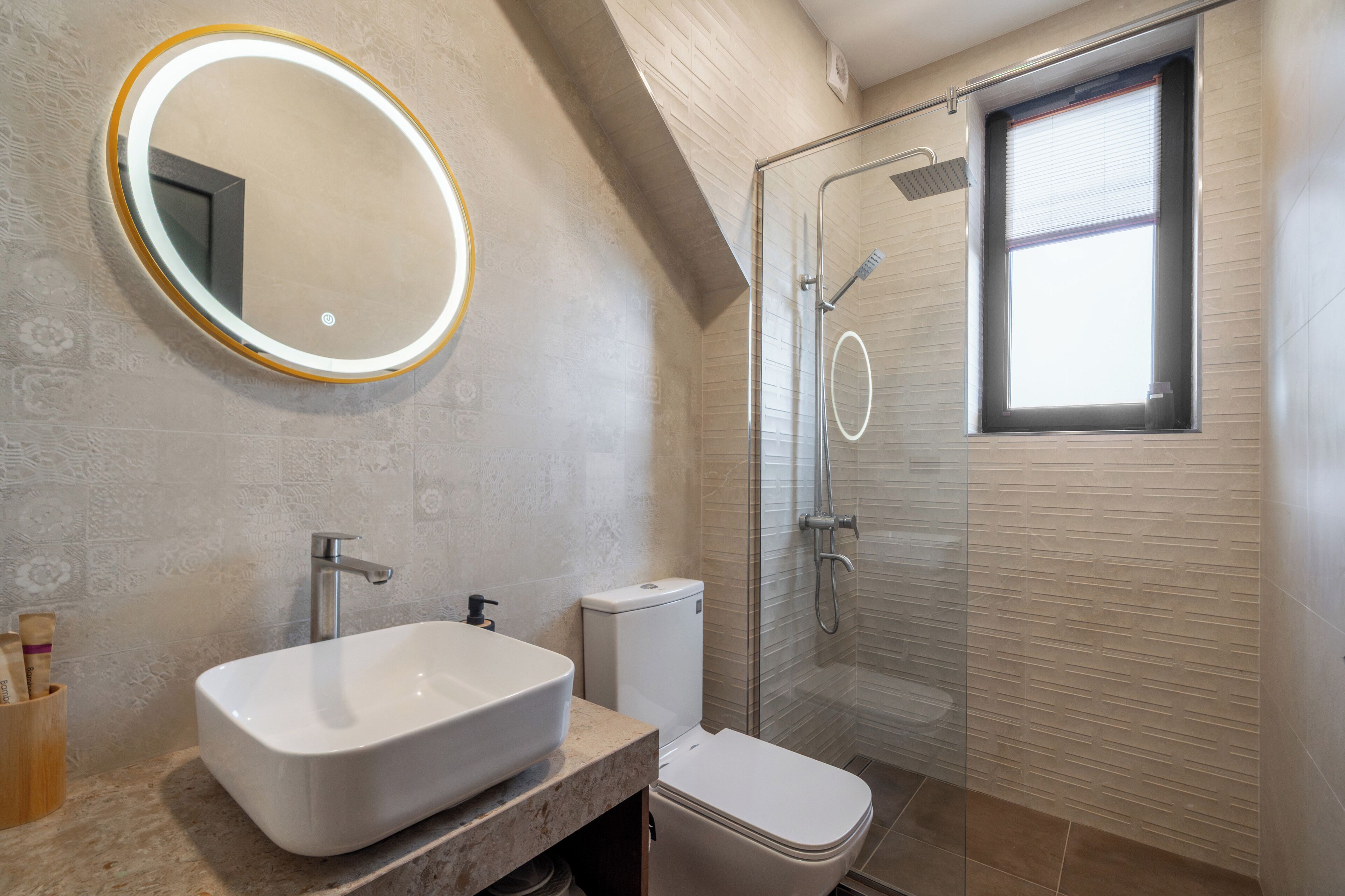 Un baño con un espejo ovalado grande, un lavamanos rectangular, un inodoro y una ducha con cerramiento de vidrio.