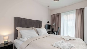 A neatly made bed with a beige quilt, a bedside lamp, and a TV on a stand. - Modern Apartment | Private Garden and Parking (Gdańsk)