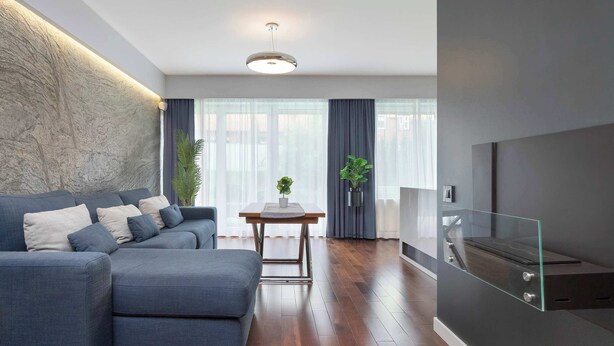 A modern living room with a sectional sofa, a dining table, and a TV mounted on a glass panel. - Modern Apartment | Private Garden and Parking (Gdańsk)