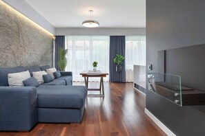 Ein modernes Wohnzimmer mit einem Ecksofa, einem Esstisch und einem an einer Glasplatte befestigten Fernseher.