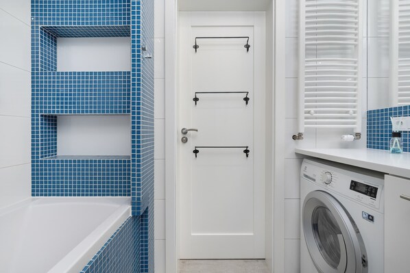 A bathroom with a white door, blue tiled walls, a white bathtub, and a washing machine.