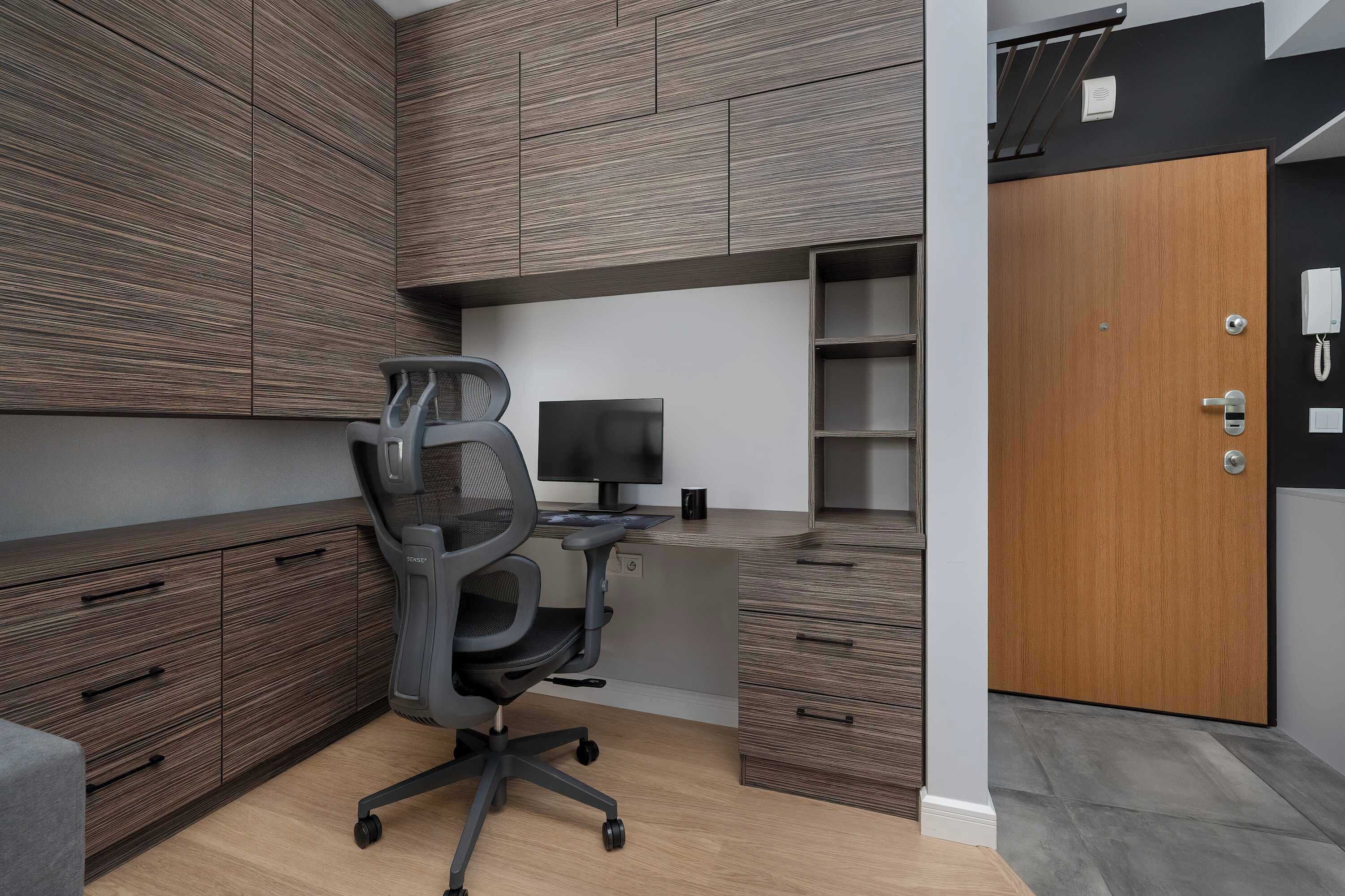 A modern office space with a desk, chair, computer, and built-in cabinets.