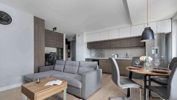 Una sala moderna con un sofá gris, una mesa de centro de madera y un comedor con una mesa redonda y sillas.