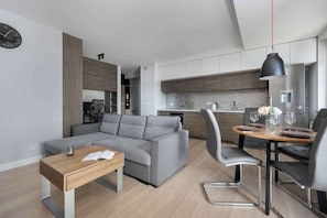 A modern living room with a grey sofa, a wooden coffee table, and a dining area with a round table and chairs.