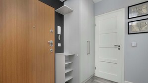 Un pasillo con una puerta de madera, una puerta blanca y una pared blanca con un teléfono y un mapa enmarcado.