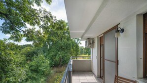 Un balcón con vistas a un paisaje verde exuberante, un banco de madera y una mesa con un vaso.