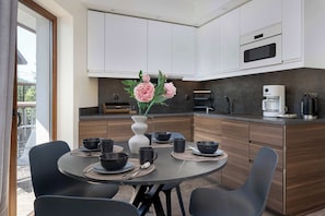A modern kitchen with white cabinets, a dining table with black chairs, and a vase with flowers.