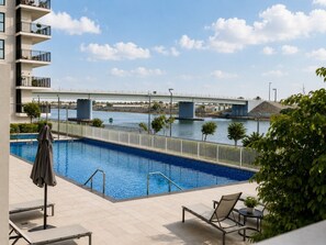 A swimming pool with a view of a bridge, lounge chairs, and a building with balconies.