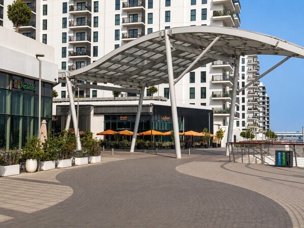 A modern building with a covered outdoor area, a restaurant with outdoor seating, and a sign for 'Pasticcio.'