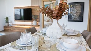 Une table à manger dressée avec de la vaisselle en verre transparent, des assiettes blanches et un vase blanc contenant des fleurs séchées.