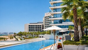 Une piscine d’hôtel offrant une vue dégagée sur la mer, des palmiers et un bâtiment moderne doté de balcons.