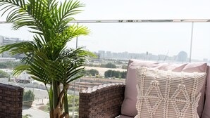 Un balcon agrémenté de meubles en osier, d’une plante en pot et offrant une vue sur le paysage urbain.