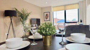 A dining table set with white plates, bowls, and wine glasses, a gold vase with green foliage, and a black floor lamp.