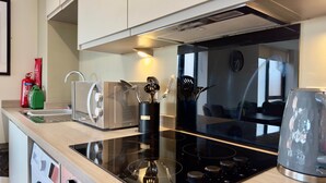 A modern kitchen with a black induction cooktop, stainless steel appliances, and a glass backsplash.