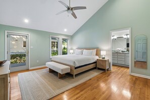 A bedroom with a bed, bedside tables, a bench, a ceiling fan, and a view of the outdoors through a door. - IOP Beach House with a Tiki Bar (Isle of Palms)