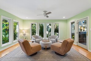 A spacious room with a ceiling fan, large windows, and a view of greenery outside. - IOP Beach House with a Tiki Bar (Isle of Palms)