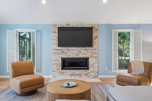 A living room with a stone fireplace, two leather armchairs, a round coffee table, and a flat-screen TV mounted above the fireplace. - IOP Beach House with a Tiki Bar (Isle of Palms)