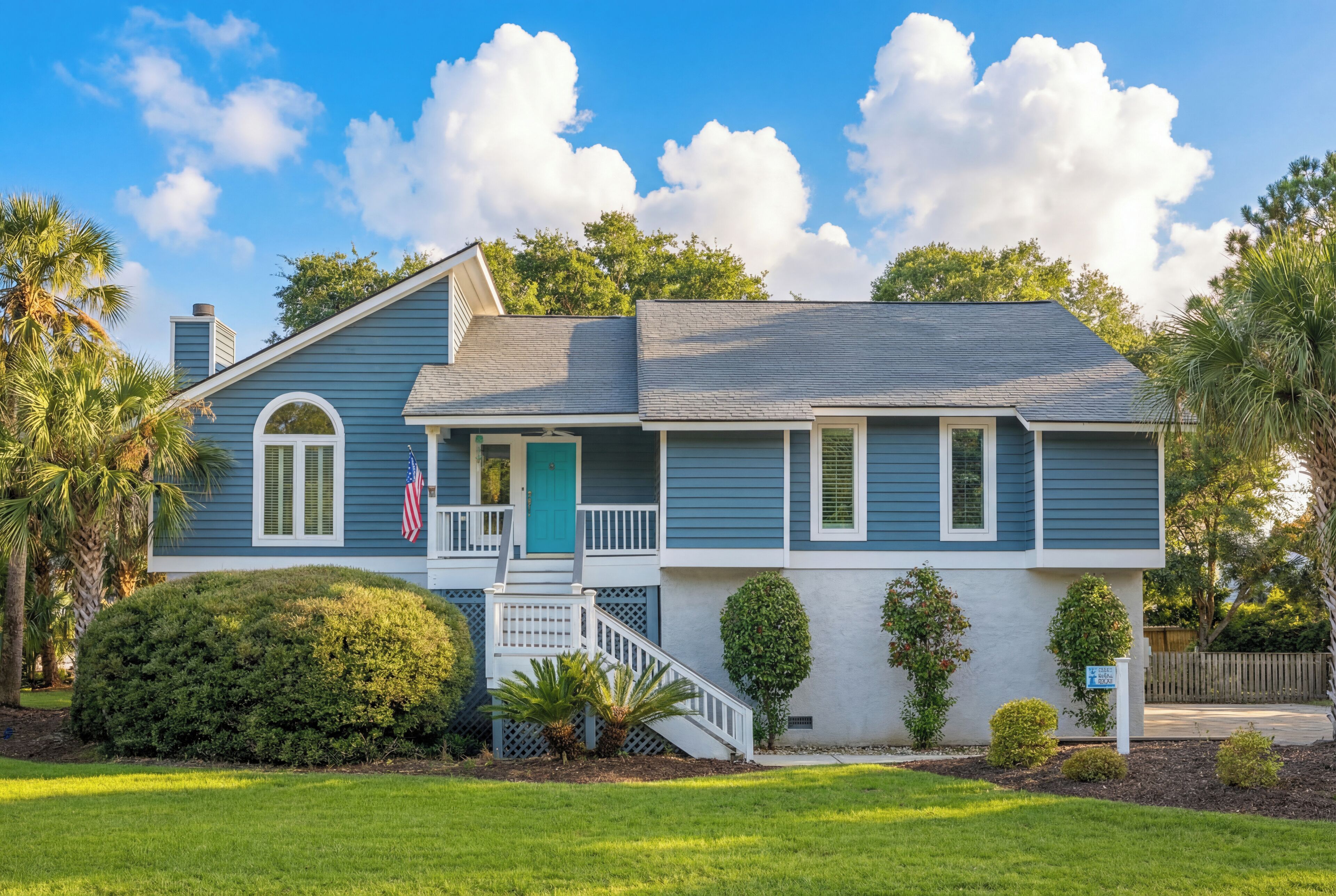 A two-story house with a front porch, a green door, and a small American flag.