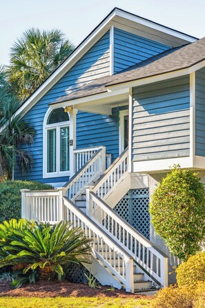 A two-story house with a front porch, a staircase, and a small garden with palm trees. - IOP Beach House with a Tiki Bar (Isle of Palms)