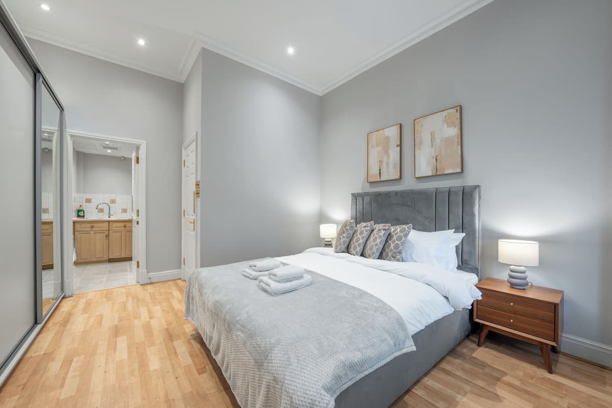 A bedroom with a bed, bedside tables, a mirror, and a view into the bathroom.