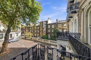 Un immeuble à plusieurs étages doté d’une façade de style traditionnel, avec un arbre au premier plan et une zone de stationnement.