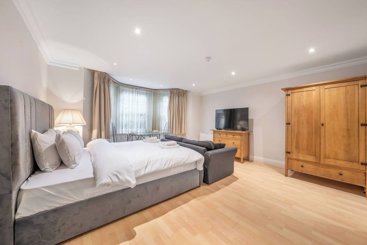 A modern bedroom with a large bed, a TV, a wardrobe, and a desk with a lamp.