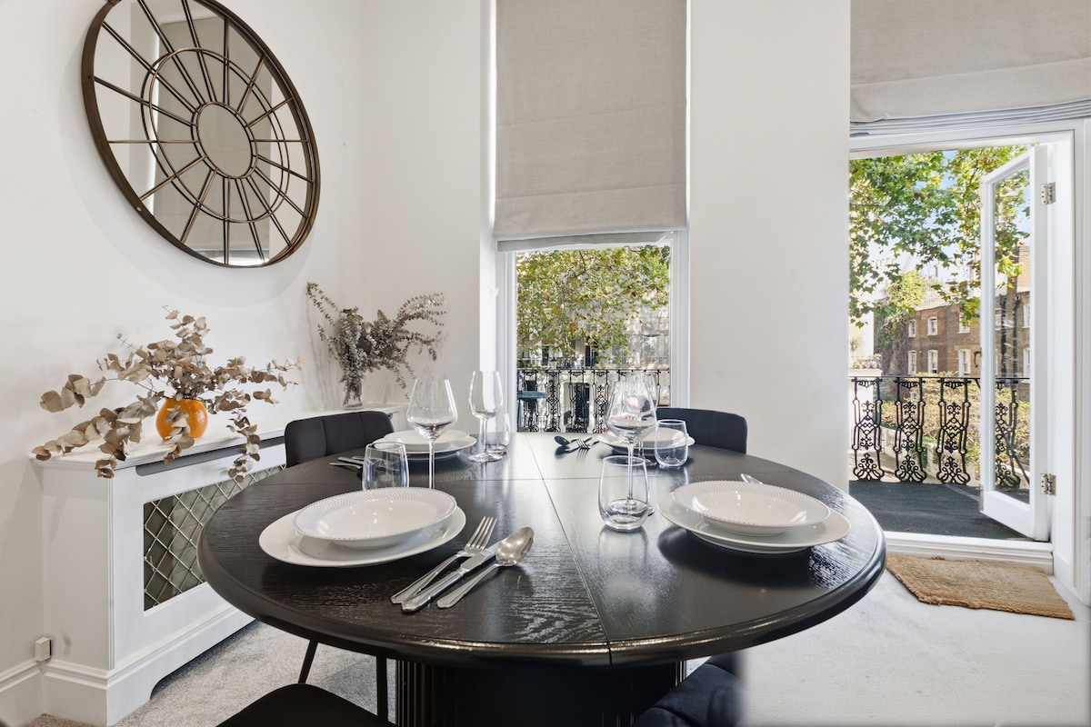 Comedor con una mesa redonda dispuesta para cuatro, sillas y un espejo decorativo en la pared.