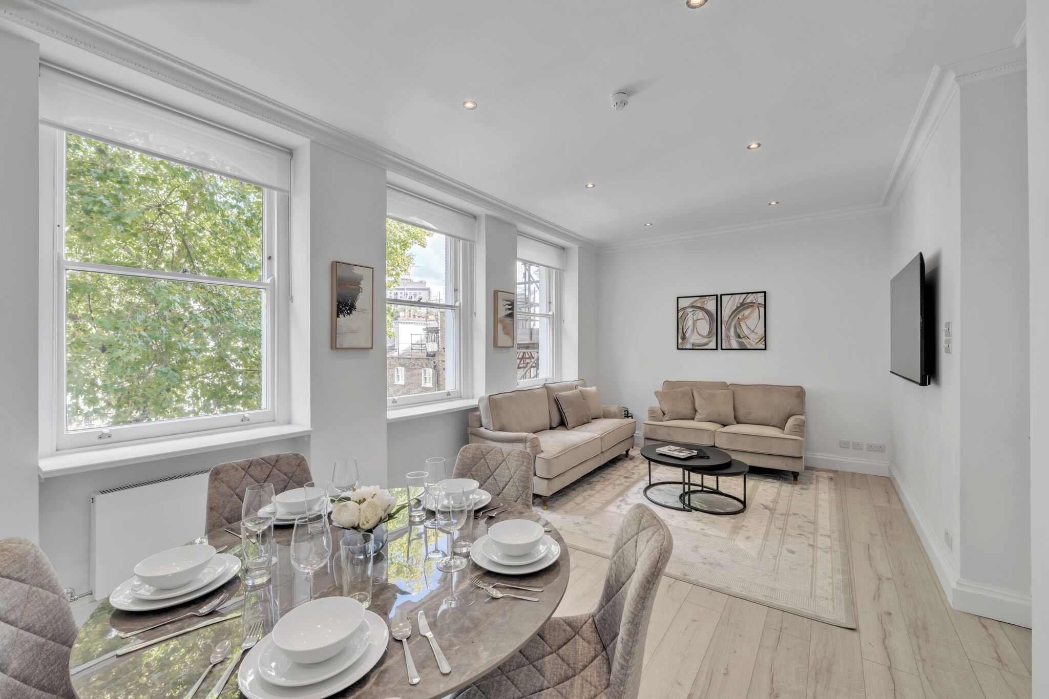 A modern living room with a large window, a sofa, a TV, and a dining area with a table set for four.
